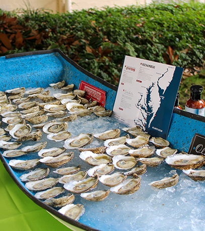 Dose-dosenang mga shucked oyster na nakaupo sa yelo sa loob ng isang asul na bangka na parang istraktura.