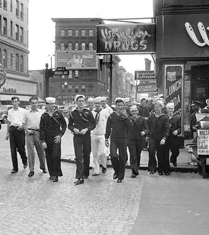Itim at puti na larawan ng 1940s era Navy sailors na naglalakad sa isang city street sa Norfolk, Virginia.