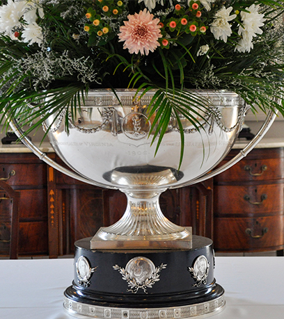 Isang silver punch bowl na puno ng floral arrangement sa isang puting table cloth.