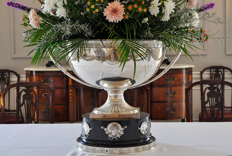 Silver punch bowl na puno ng floral arrangement na nakapatong sa puting table cloth.